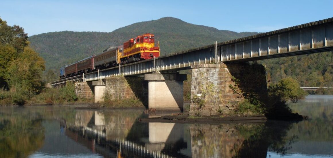 a2ab4405-5ad9-4bab-96b7-03547e0a1810-mirrored-train-crossing-hiwassee-river-mountain-in-backgroun