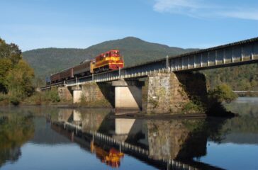 a2ab4405-5ad9-4bab-96b7-03547e0a1810-mirrored-train-crossing-hiwassee-river-mountain-in-backgroun