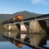 a2ab4405-5ad9-4bab-96b7-03547e0a1810-mirrored-train-crossing-hiwassee-river-mountain-in-backgroun